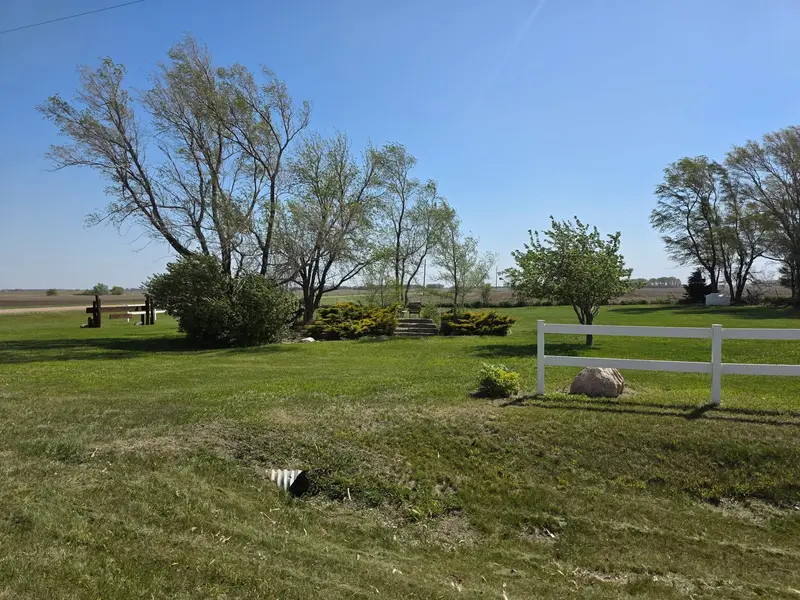 A large mown country yard with trees and a white rail fence