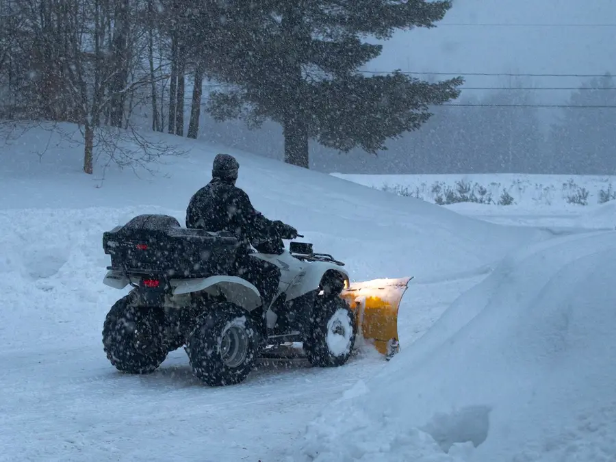 A four-wheeler with a plow blade pushing snow off a driveway