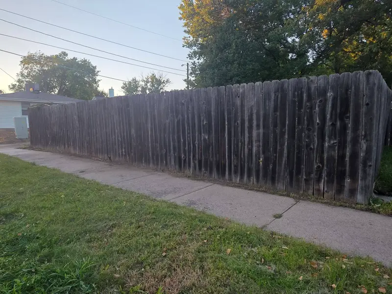 A mown strip of lawn running along a tall wooden fence and a sidewalk