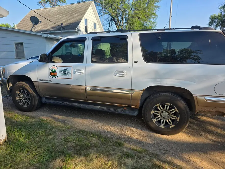 The OH Lawn Care GMC Yukon XL parked on a lawn beside a Mount Vernon home