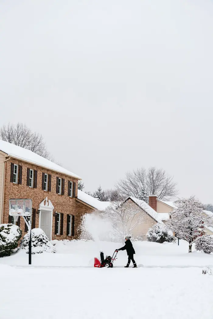 A snowblower clearing the driveway in front of a house after a snowfall